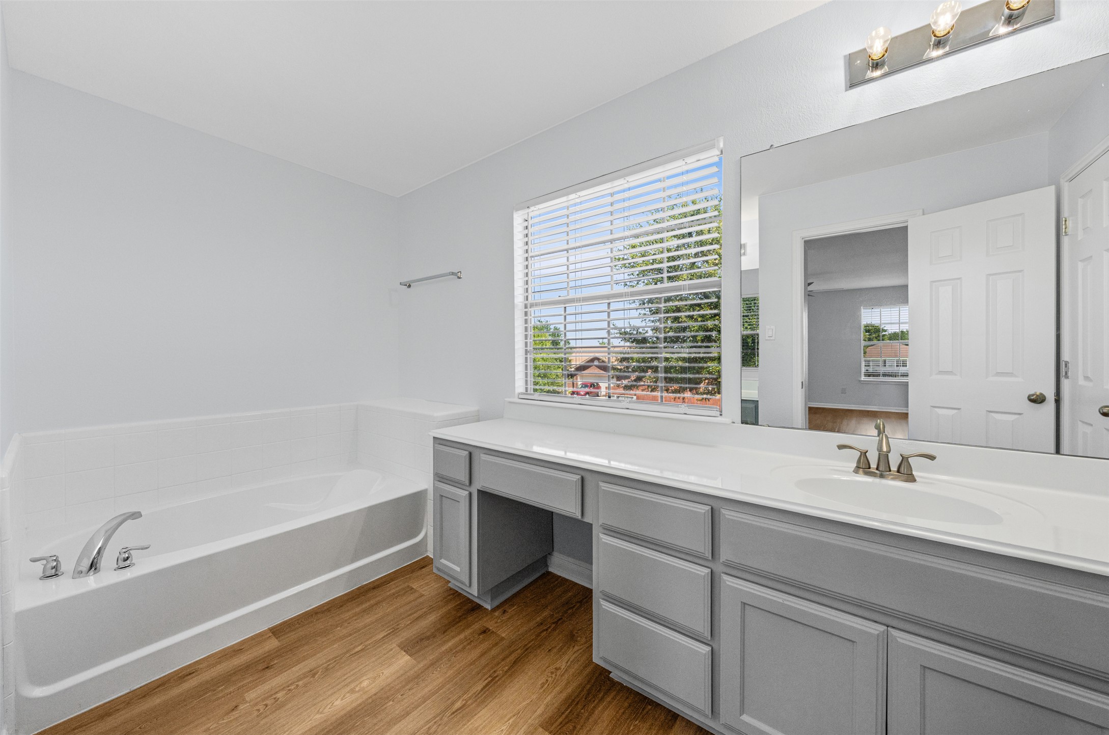 243 Engineers Pass Jarrell, TX 76537 - Photo 21 of 40 Bathroom featuring a white built-in bathtub, a window with blinds, a vanity with a white countertop and integrated sink, gray cabinetry, and wood-finish flooring