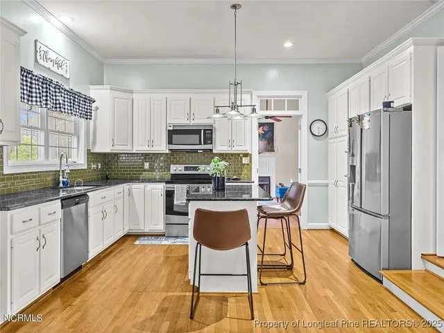 a kitchen with stainless steel appliances granite countertop a refrigerator a stove top oven a sink dishwasher and white cabinets with wooden floor