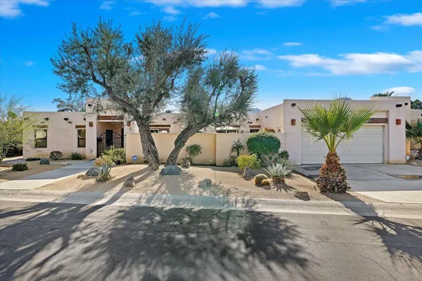 a view of a white house with large trees and flower plants