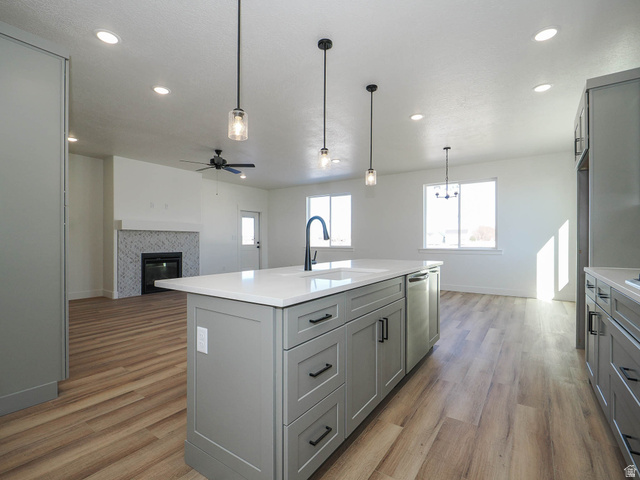 3938 North Wood Road Eagle Mountain, UT 84005 - Photo 54 of 55 Kitchen with gray cabinetry, a tiled fireplace, open floor plan, light wood-style floors, and pendant lighting