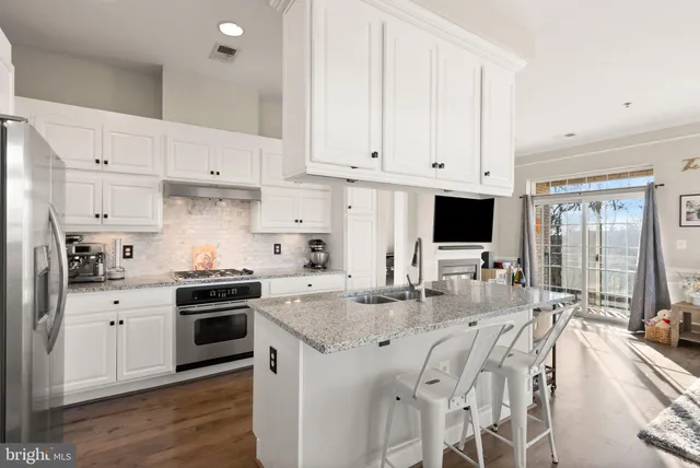 a kitchen with stainless steel appliances granite countertop a stove a sink dishwasher and a refrigerator with white cabinets