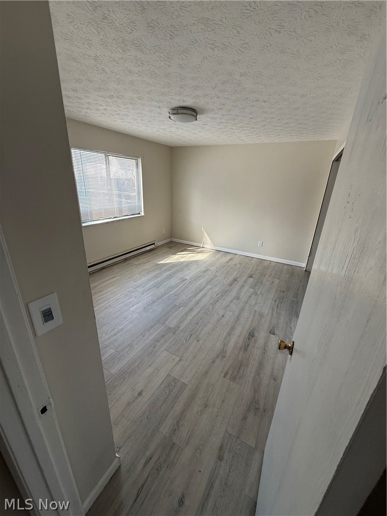 662 Sumner Street Akron, OH 44311 - Photo 7 of 10 Unfurnished room featuring light wood-type flooring, a textured ceiling, and a baseboard radiator