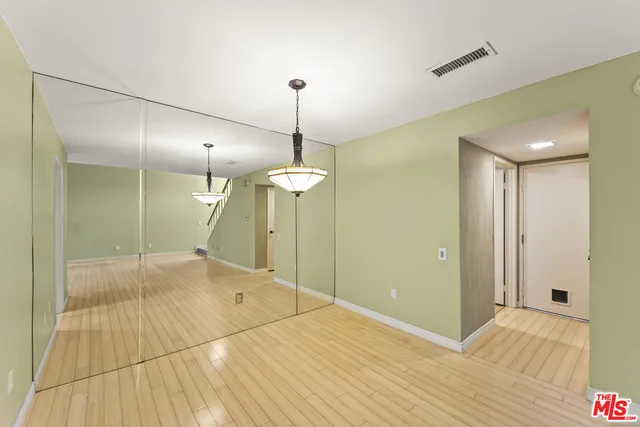 a view of an empty room with wooden floor and a kitchen