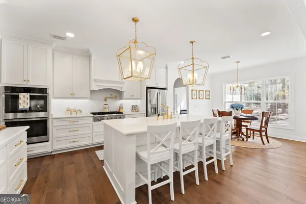 a kitchen with stainless steel appliances kitchen island granite countertop a dining table chairs stove and white cabinets