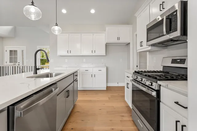 a kitchen with stainless steel appliances granite countertop a stove top oven a sink dishwasher and white cabinets with wooden floor