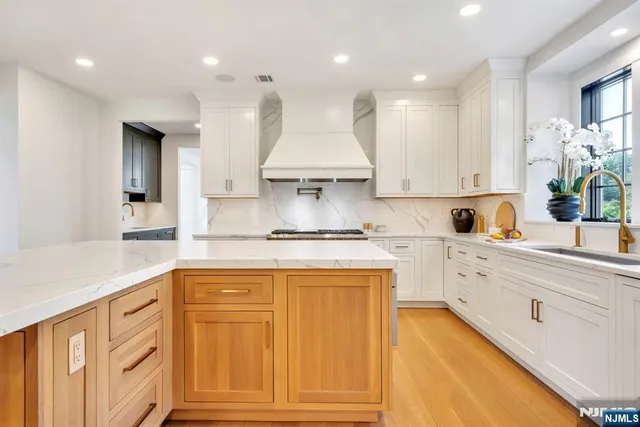 a large kitchen with stainless steel appliances granite countertop a stove a sink dishwasher and white cabinets with wooden floor