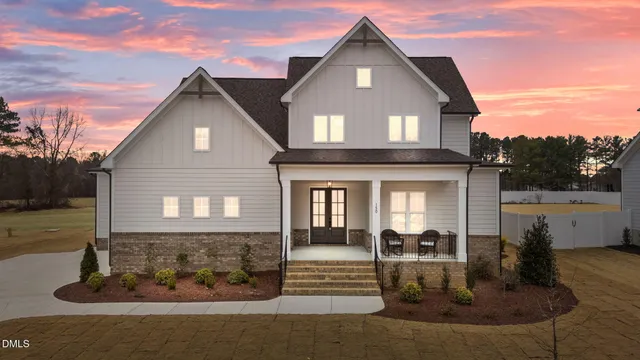 a view of a white house next to a yard with potted plants