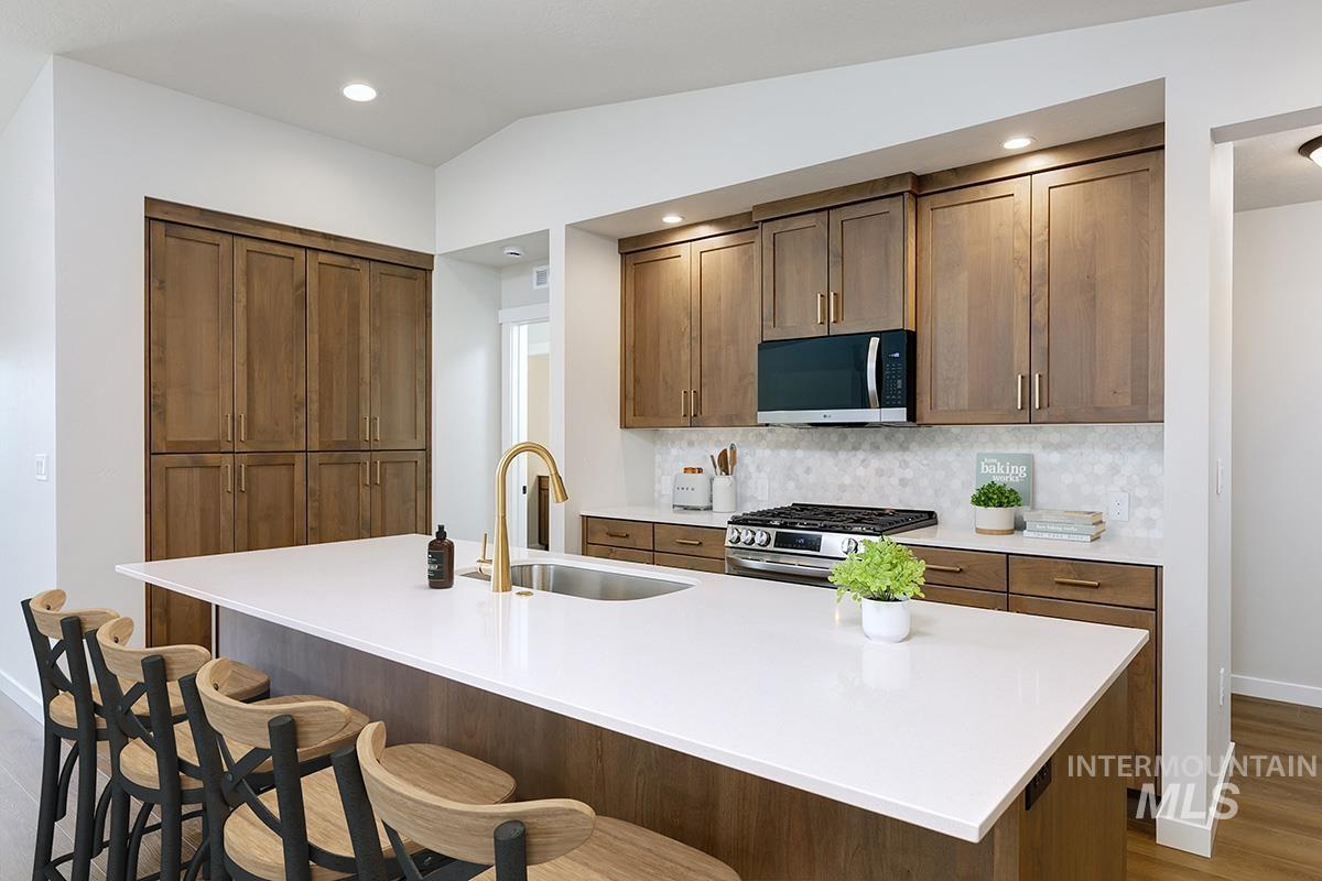 1700 East Hadler Street Meridian, ID 83642 - Photo 5 of 25 Kitchen featuring a kitchen breakfast bar, stainless steel gas range, decorative backsplash, wood finish cabinetry, and dark wood-style flooring