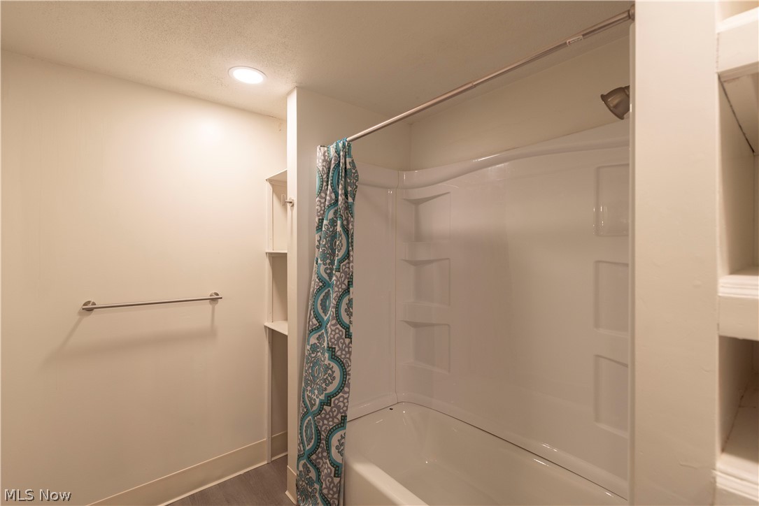 1022 North Howard Street Akron, OH 44310 - Photo 31 of 38 Bathroom featuring luxury vinyl flooring, shower / bath combination with curtain, built-in shelving for storage, and a textured ceiling with LED light fixtures.