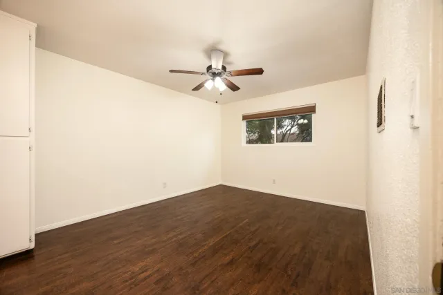 an empty room with wooden floor fan and windows