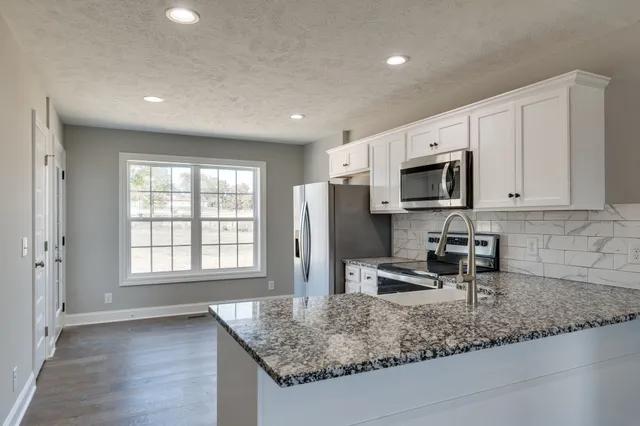 a kitchen with stainless steel appliances granite countertop a sink a microwave a refrigerator and white cabinets