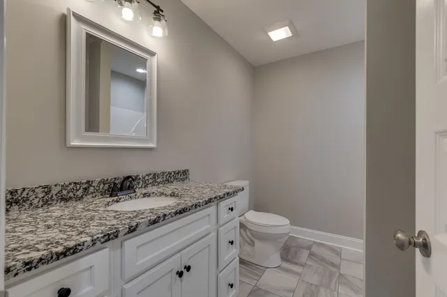a bathroom with a granite countertop sink a toilet and a mirror