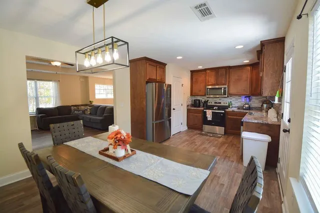 a kitchen with stainless steel appliances granite countertop a refrigerator a stove top oven a dining table and chairs a oven with wooden floor