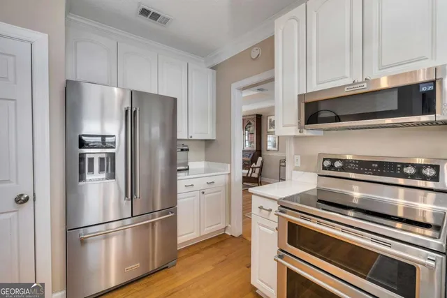 a open kitchen with stainless steel appliances granite countertop a refrigerator a oven a sink a stove and white cabinets with wooden floor