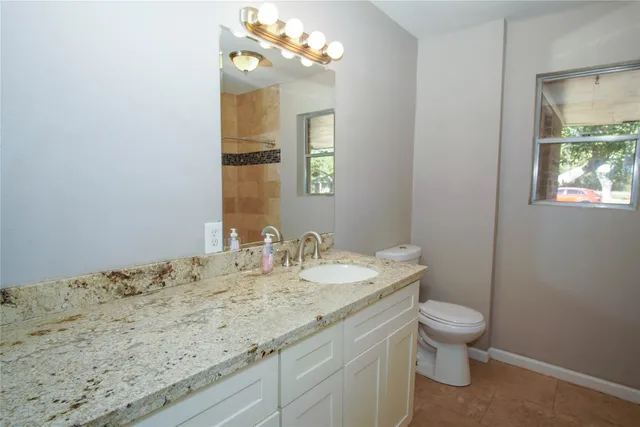 a bathroom with a granite countertop sink a toilet and a mirror