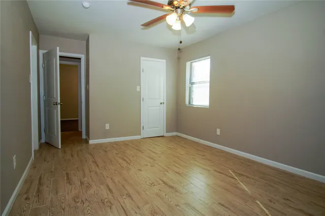 an empty room with wooden floor fan and windows
