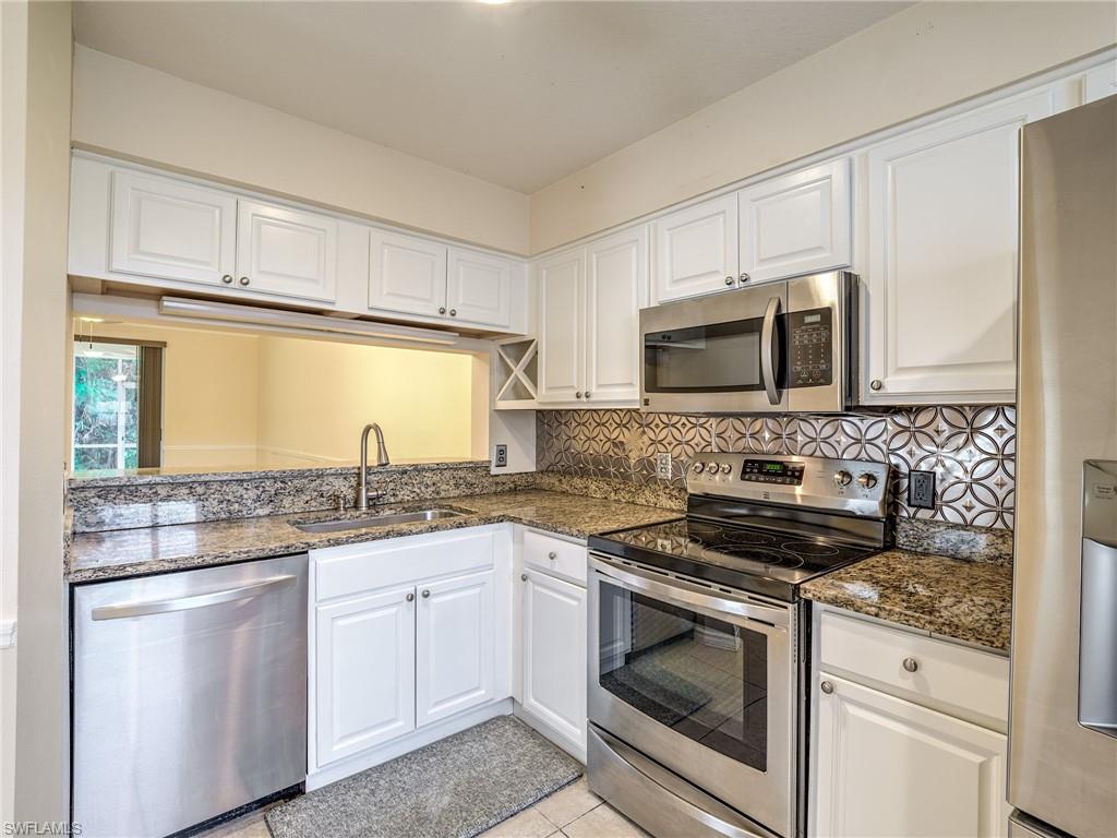 a kitchen with granite countertop white cabinets white stainless steel appliances and a sink