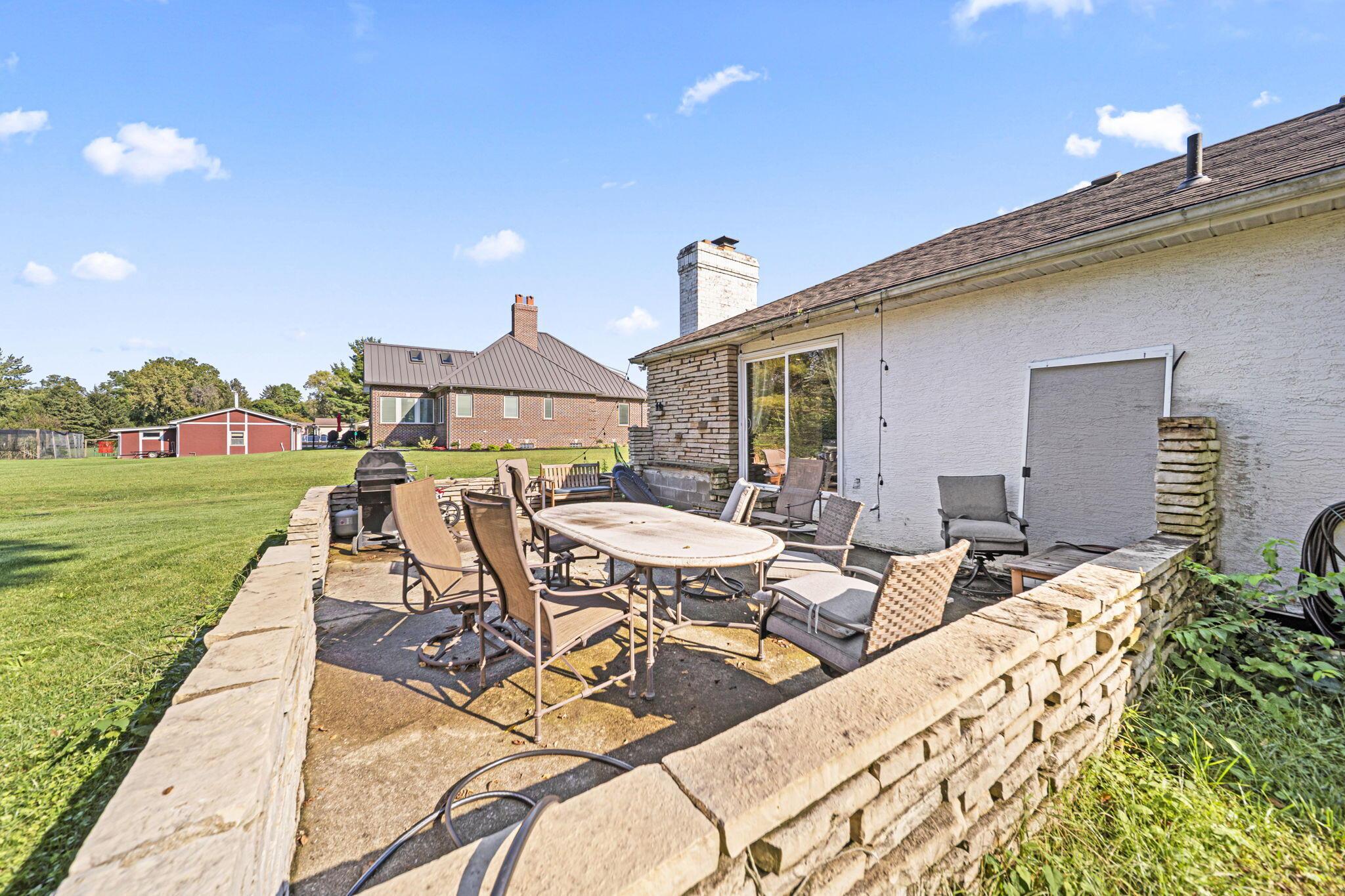 6344 Post Road Dublin, OH 43017 - Photo 30 of 45 Expansive stone patio with a stone retaining wall, sliding glass door access, and a stucco exterior