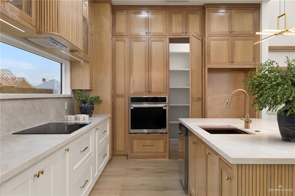 1107 Benjamin Street Mission, TX 78573 - Photo 10 of 19 Gourmet kitchen featuring extensive custom wood cabinetry, integrated stainless steel appliances, a large center island with a built-in sink, and light-toned countertops