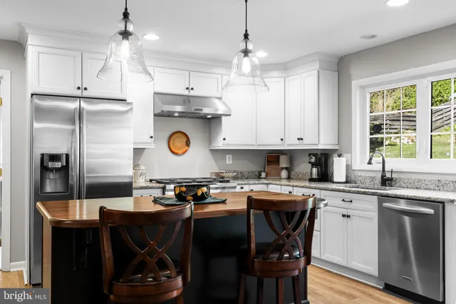 a kitchen with stainless steel appliances granite countertop a stove a refrigerator a sink dishwasher and white cabinets with wooden floor