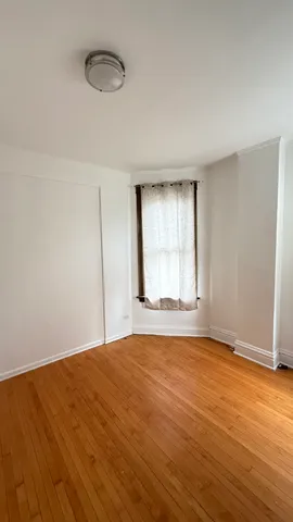 a view of an empty room with wooden floor and window
