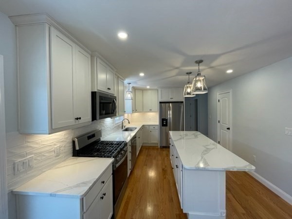 39 Staples Street Billerica, MA 01821 - Photo 4 of 25 a large kitchen with kitchen island a stove a sink a refrigerator and a dining table with wooden floor