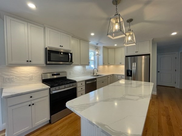 39 Staples Street Billerica, MA 01821 - Photo 9 of 25 a large kitchen with stainless steel appliances granite countertop a sink dishwasher a stove a microwave oven a refrigerator with white cabinets and wooden floor