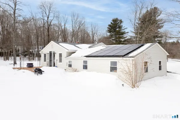 a view of a white house with a yard covered with snow and trees