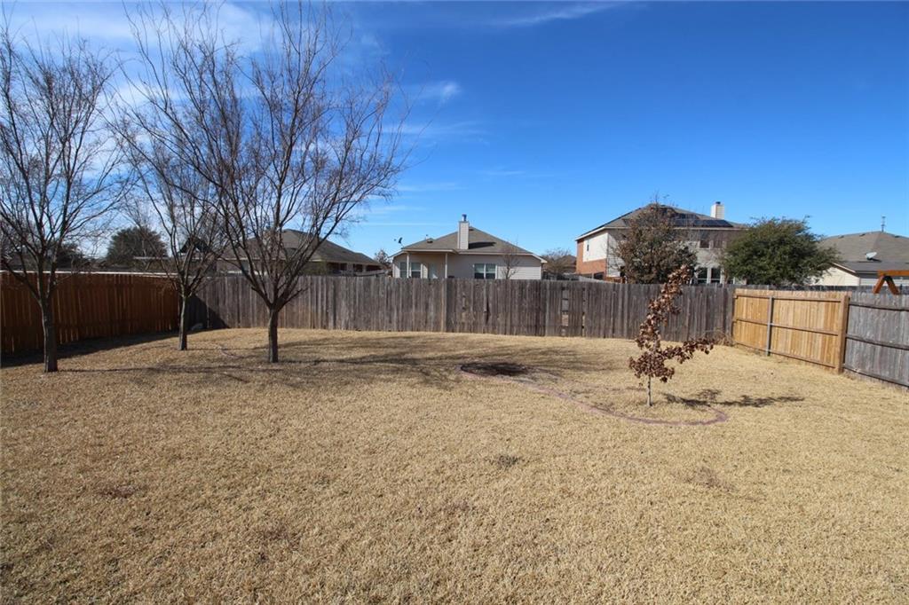 107 Inman Drive Hutto, TX 78634 - Photo 16 of 19 Expansive backyard featuring a natural grass lawn, mature trees, and a full privacy fence