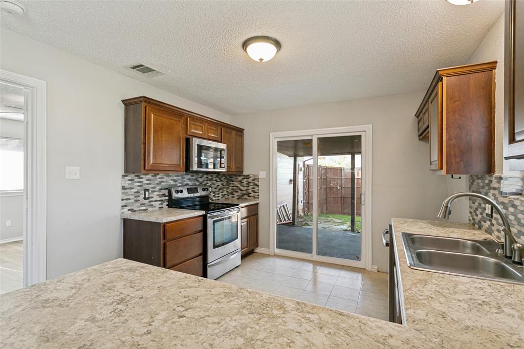 1712 East Peters Colony Road Carrollton, TX 75007 - Photo 7 of 25 Kitchen featuring rich wood cabinetry, stainless steel appliances, a mosaic tile backsplash, and durable countertops