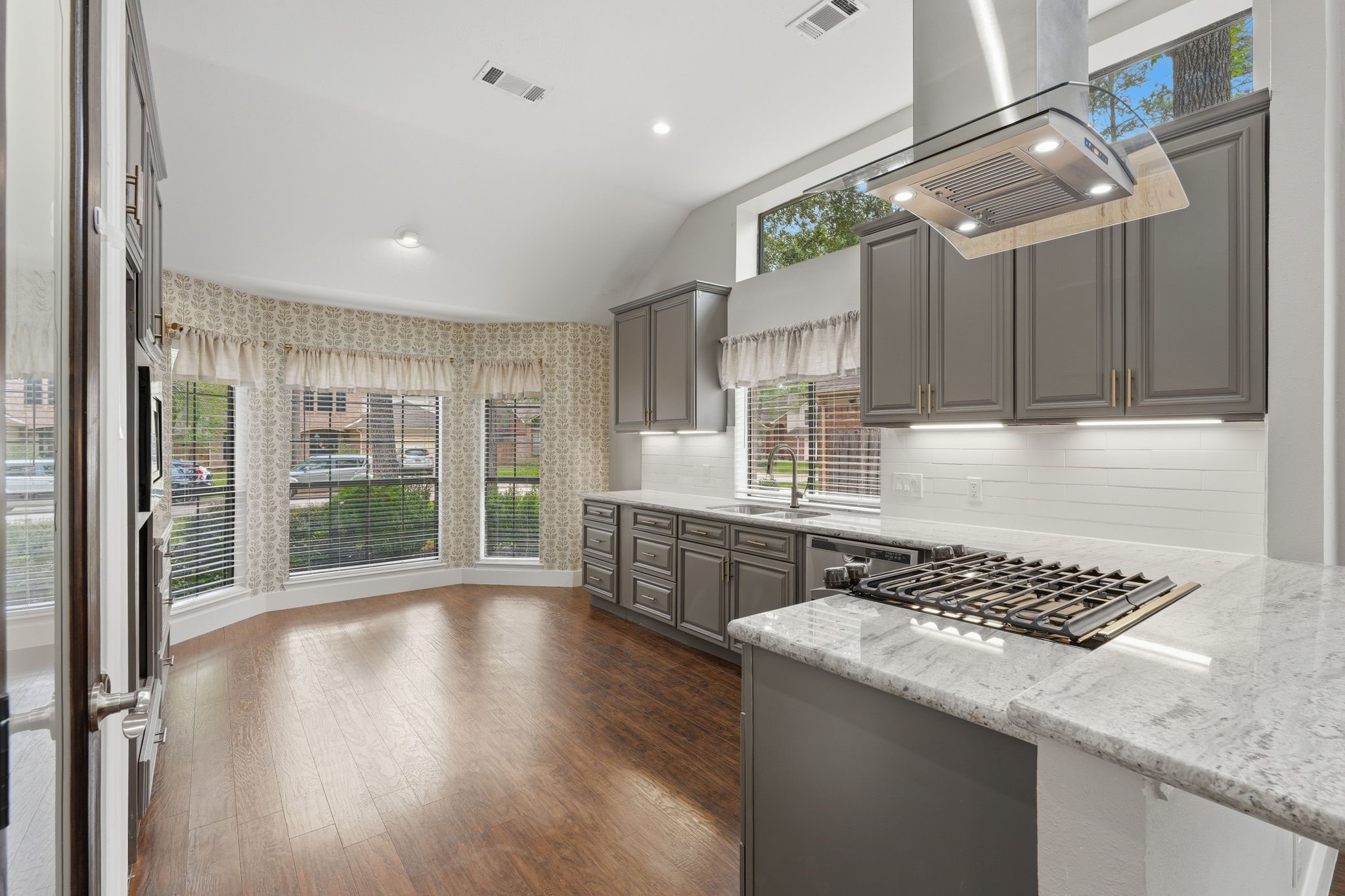 14 Dusky Meadow Place Spring, TX 77381 - Photo 13 of 47 Light-filled kitchen with granite countertops, gas cooktop, and custom vent hood. Vaulted ceiling and expansive windows highlight the spacious breakfast area and inviting design.