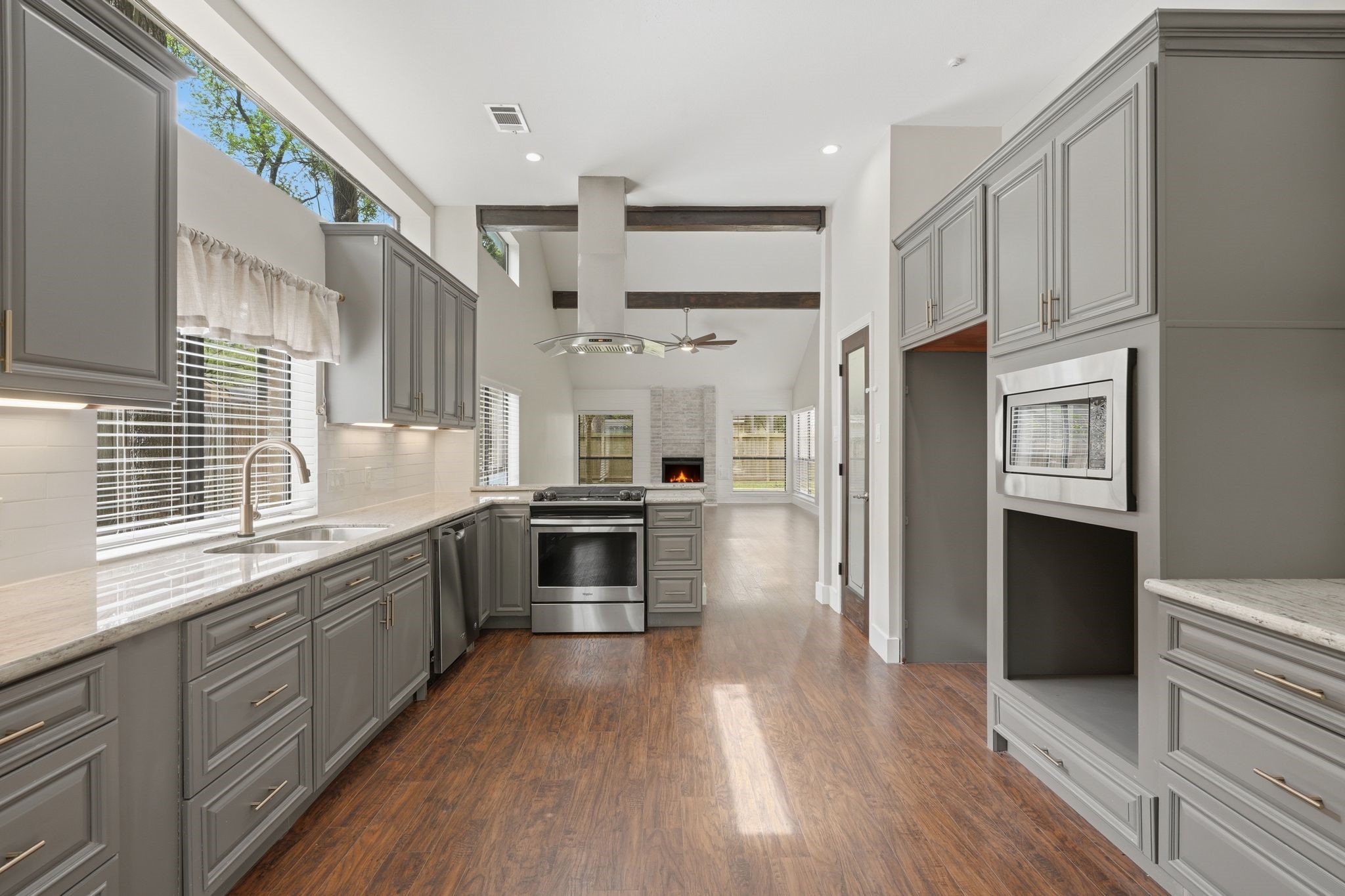 14 Dusky Meadow Place Spring, TX 77381 - Photo 15 of 47 Spacious open-concept kitchen with granite countertops, gas cooktop, and abundant cabinetry, flowing seamlessly into the living area with exposed beams and fireplace—perfect for everyday living and entertaining.