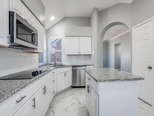 a kitchen with granite countertop a sink stainless steel appliances white cabinets and window
