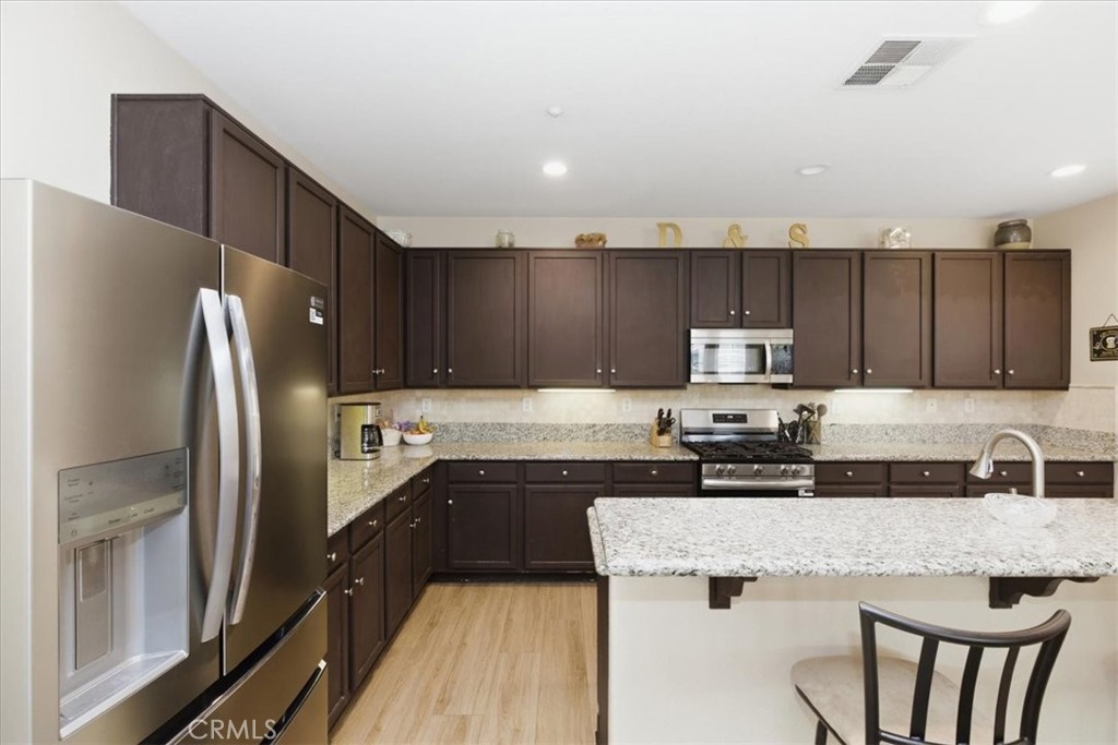 7353 Ellena West, Unit 70 Rancho Cucamonga, CA 91730 - Photo 18 of 40 a kitchen with kitchen island granite countertop a refrigerator a sink a stove a microwave and island with wooden floor
