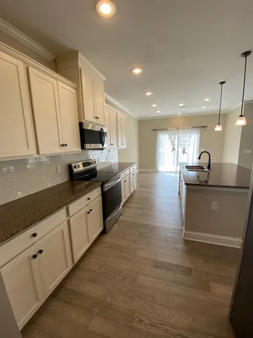 a large white kitchen with stainless steel appliances granite countertop a stove a sink a refrigerator white cabinets and wooden floor