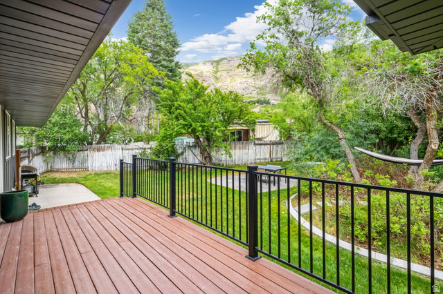 4150 Dover Lane Provo, UT 84604 - Photo 35 of 44 Expansive wood-finish deck with black metal railings, overlooking a verdant backyard with mature trees and a fenced perimeter
