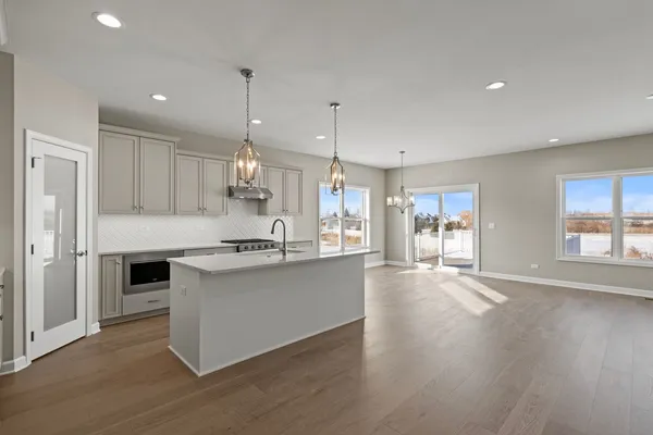 a large kitchen with granite countertop a stove a sink a refrigerator and white cabinets with wooden floor