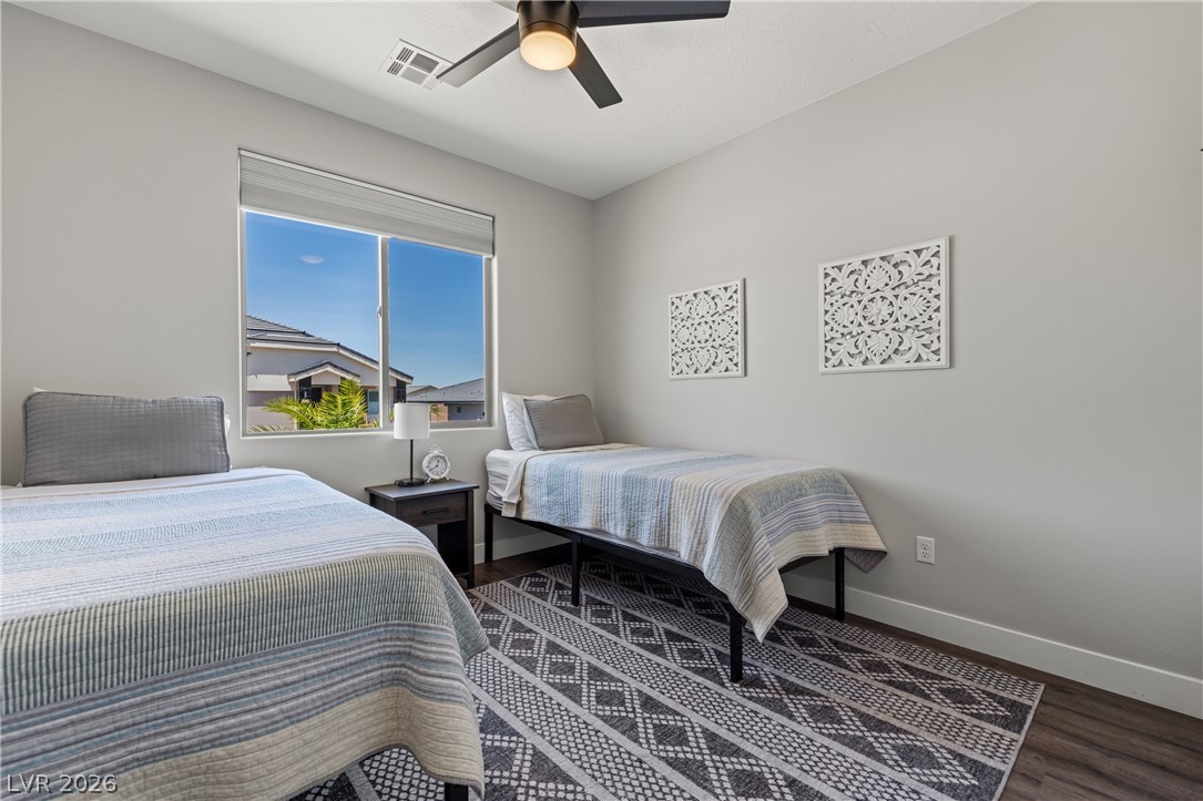 1436 Manassas Ridge Mesquite, NV 89027 - Photo 7 of 77 A comfortable bedroom with rich wood flooring and a modern ceiling fan, offering a pleasant view of the neighborhood.