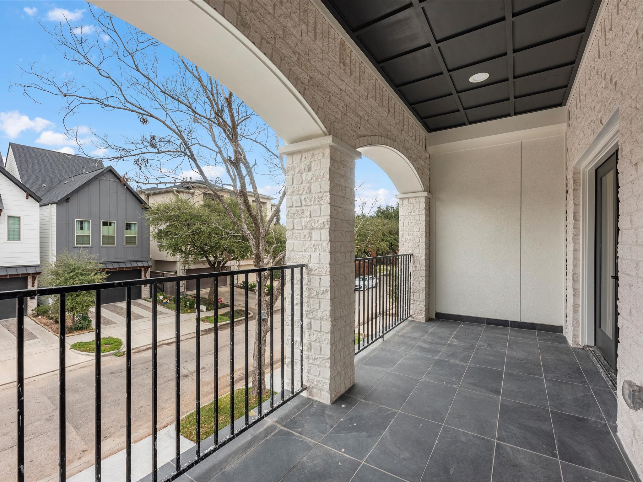 1319 West Bell Street Houston, TX 77019 - Photo 24 of 50 This photo showcases a spacious, covered balcony with elegant arched openings and a tiled floor, offering a pleasant view of a quiet residential street lined with trees and modern homes.