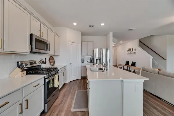 a kitchen with stainless steel appliances a stove top oven a sink a refrigerator white cabinets and wooden floor