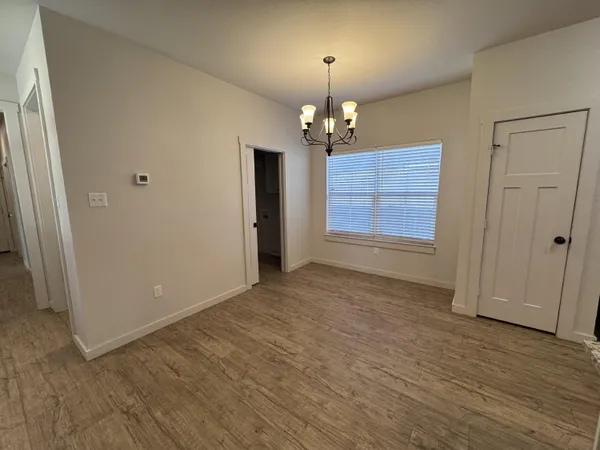 an empty room with wooden floor chandelier and refrigerator