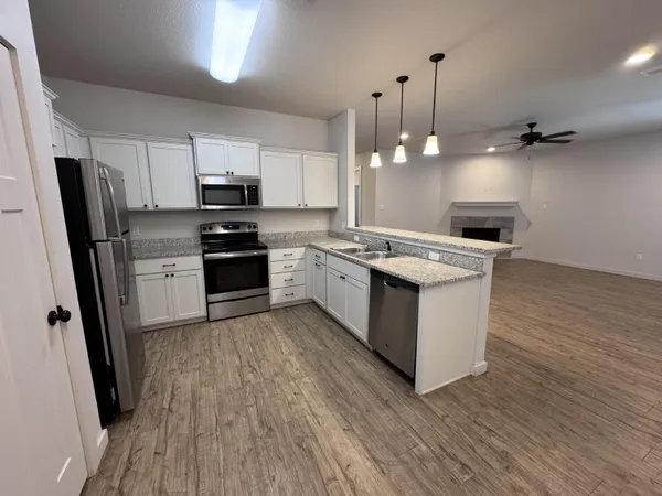 a kitchen with stainless steel appliances granite countertop a stove top oven a sink dishwasher a refrigerator and a dining table with wooden floor