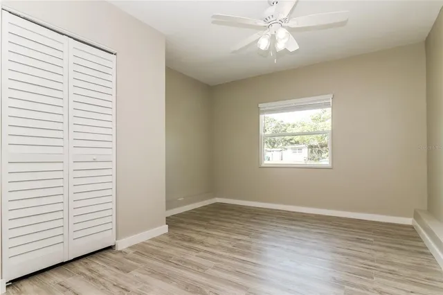an empty room with wooden floor chandelier fan and windows