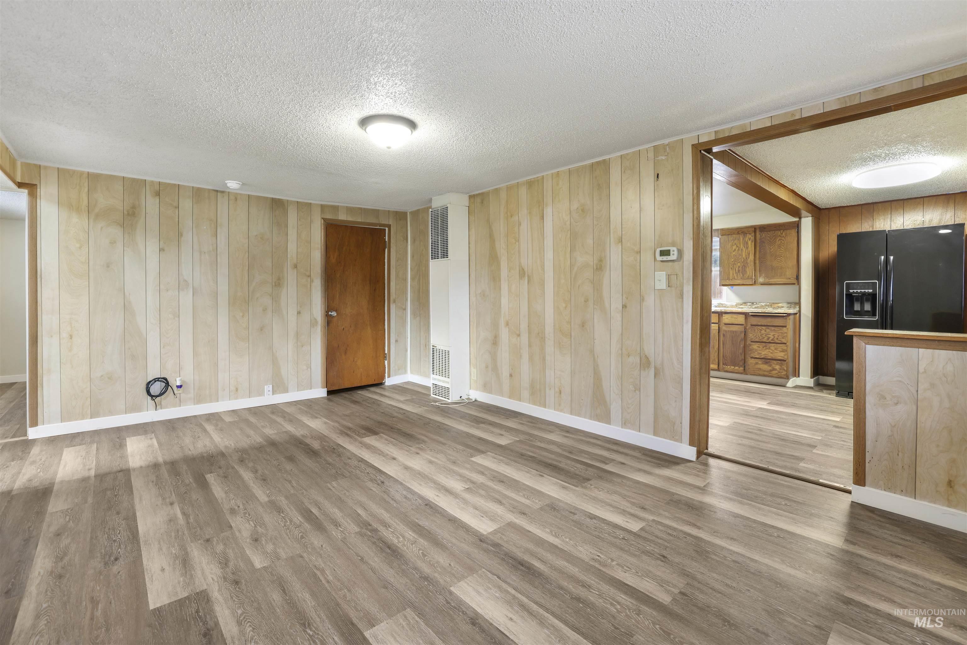 545 Madison Street Twin Falls, ID 83301 - Photo 10 of 23 Unfurnished living room with wood walls, a textured ceiling, light wood-style flooring, and a heating unit