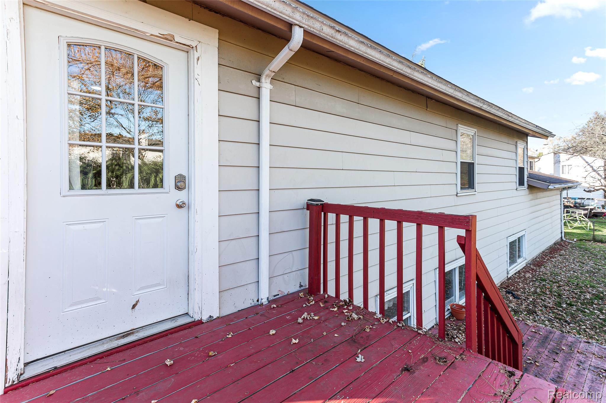 22582 Winfield Road Novi, MI 48375 - Photo 35 of 37 Exterior deck with red-painted wood flooring and railings, featuring direct access via a white door with an arched window insert
