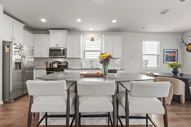a kitchen with white cabinets a sink a stove a dining table and chairs