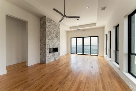 a big room with wooden floor a ceiling fan and windows
