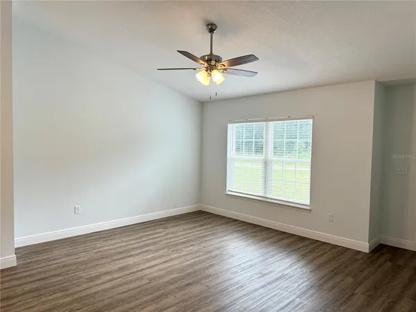 an empty room with wooden floor chandelier fan and windows