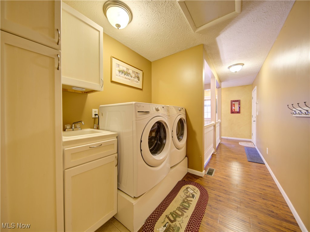 17161 Burrows Road Thompson, OH 44086 - Photo 24 of 48 Laundry room featuring sink, light hardwood / wood-style flooring, cabinets, a textured ceiling, and washing machine and clothes dryer