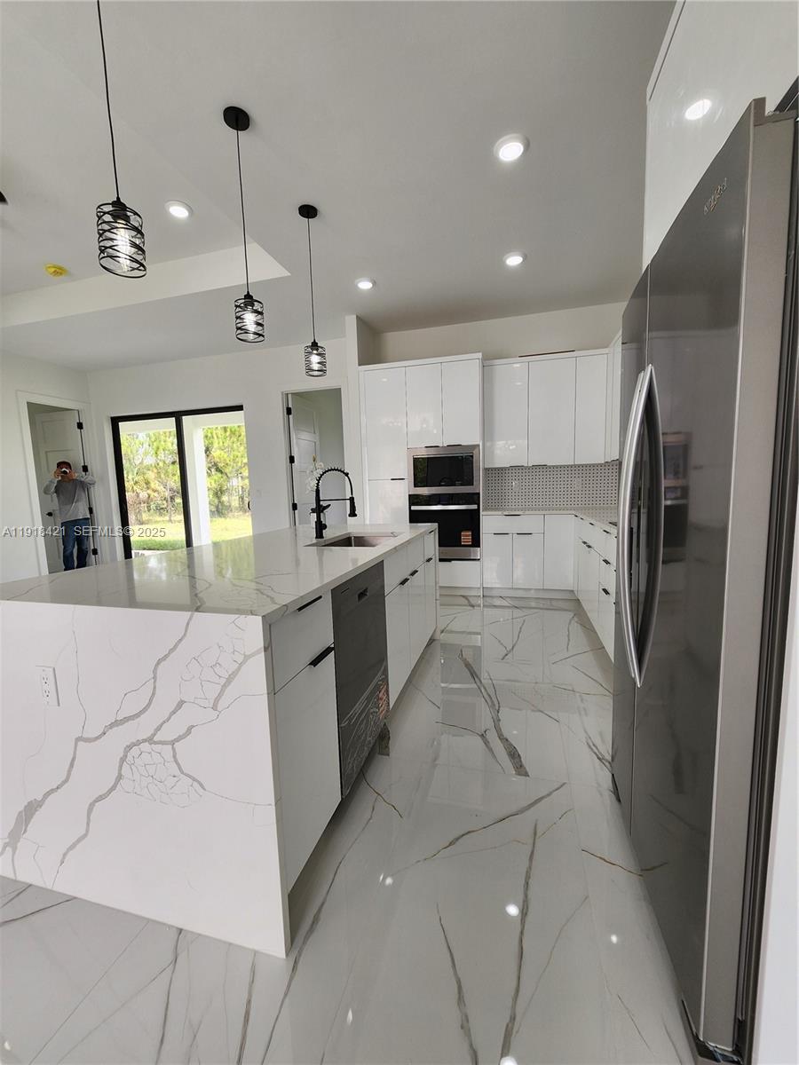 3302 East 18th Street, Unit ST Lehigh Acres, FL 33972 - Photo 9 of 34 a large kitchen with stainless steel appliances kitchen island granite countertop a refrigerator a sink a stove and white cabinets